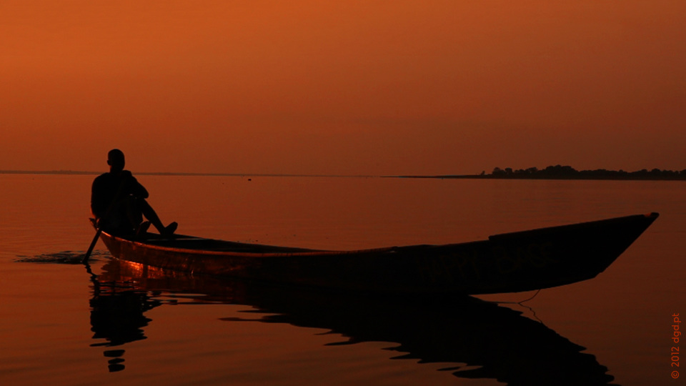 fisherman in wooden canoe boat paddling toward shore during sunset on lake volta in ghana africa